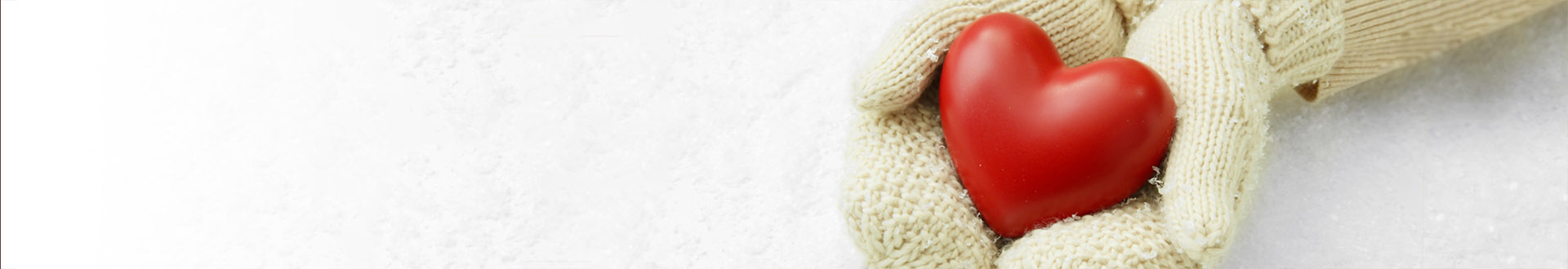 Zwei behandschuhte Hände halten ein kleines rotes Herz aus Holz über eine schneebedeckte Fläche. Vermittelt wird ein Gefühl von sozialer Fürsorge, Wärme und Nächstenliebe.